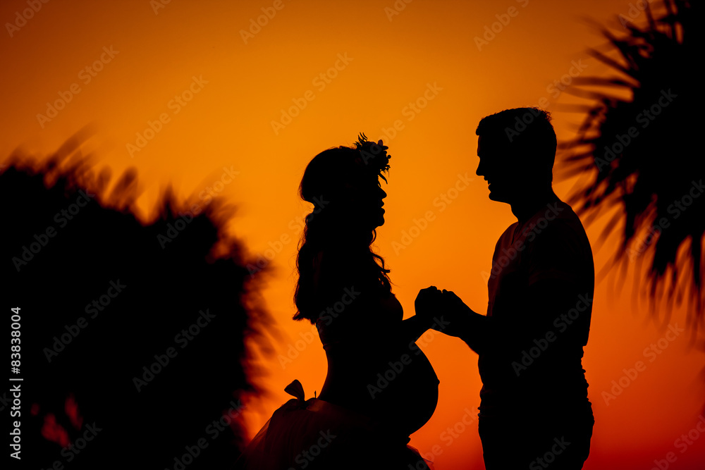Silhouette of young couple expecting baby holding hands during s