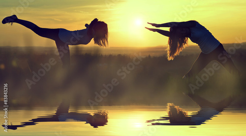Silhouette girls stretching on a meadow at sunset