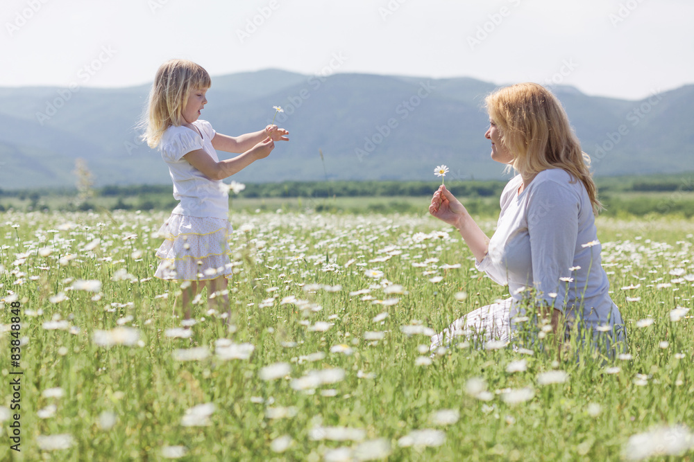 Fototapeta premium Happy mother playing with her daughter in flower field
