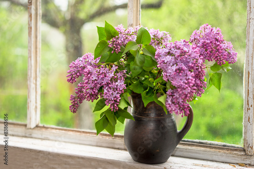 Lush bouquet of lilac in a brown clay vase on a window sill photo