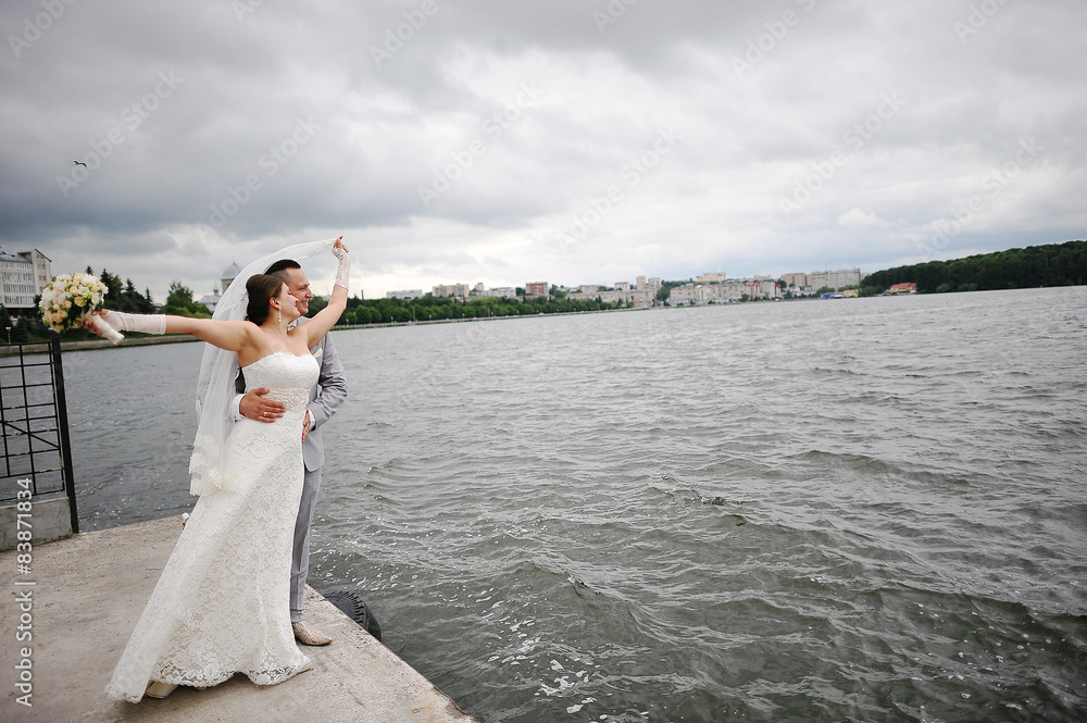 Wedding couple on the windy weather embrace near the lake Wedding couple on the windy weather embrace near the lake