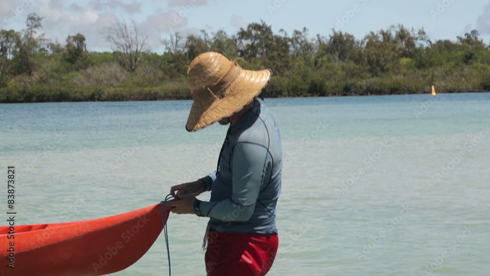 young man preparing a set of red kayaks for tourists to use. Mauritian landscape with mangroves in the background young man preparing a set of red kayaks for tourists to use. Mauritian landscape with mangroves in the background