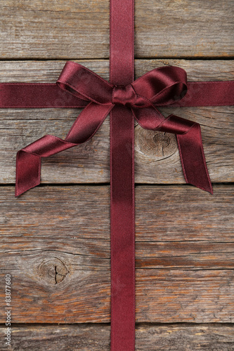 Burgundy ribbon with bow on grey wooden background