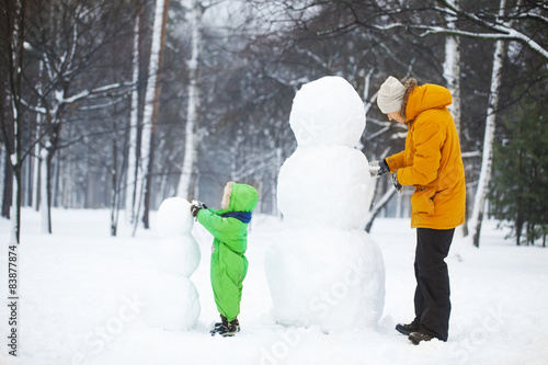 Son and father make two snowmans in park. 
