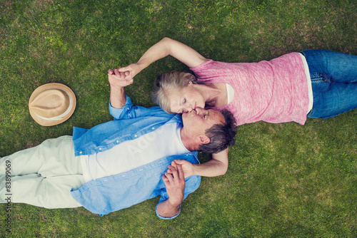 Beautiful seniors lying on a grass in a park hugging