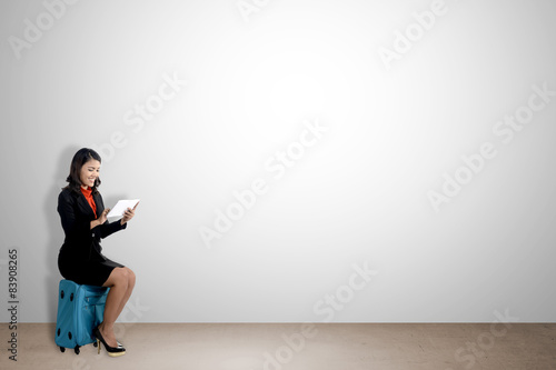 Woman sitting on suitcase looking at computer tablet