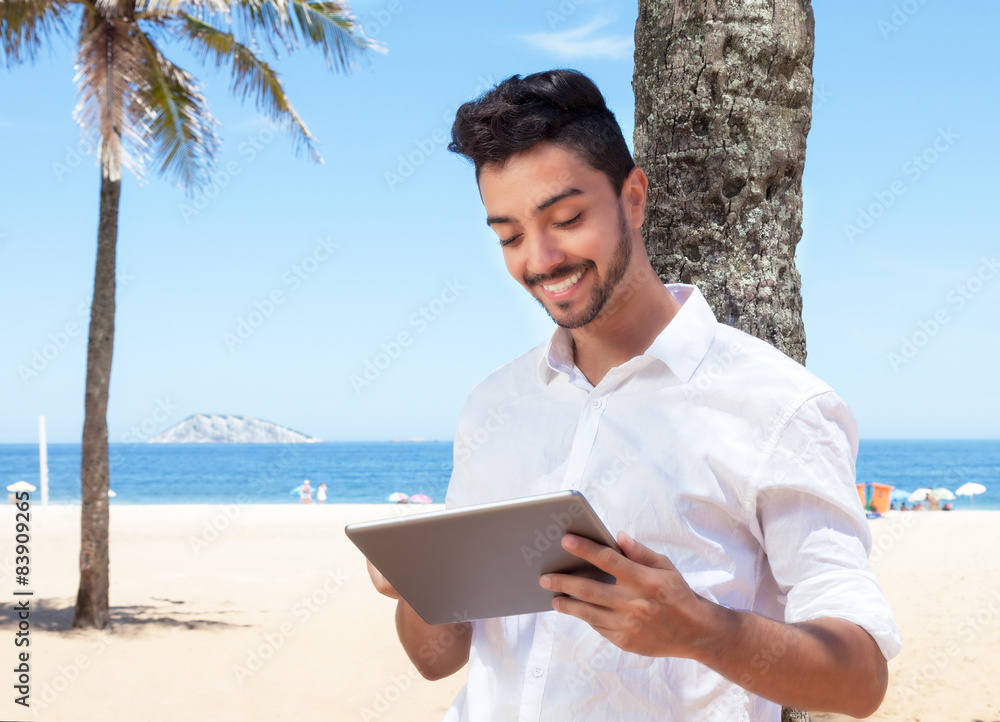 Lachender junger Mann liest E-Book am Meer