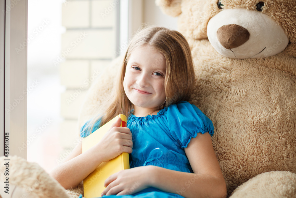 Little girl holding a book on windowsill with big toy Little girl holding a book on windowsill with big toy