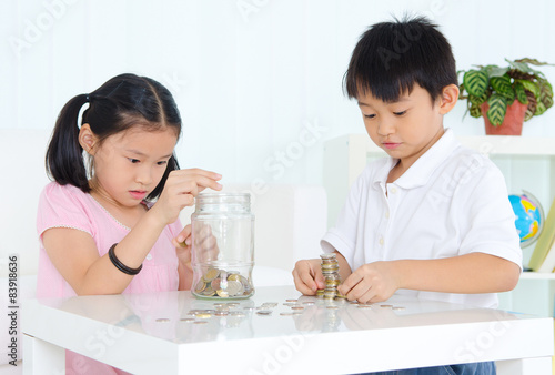 Asian kids putting coins into the glass bottle