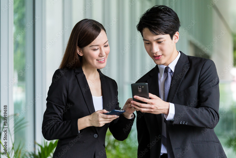 Businesswoman share something on cellphone with her colleague Businesswoman share something on cellphone with her colleague