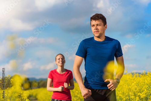 Beautiful young couple jogging outside in canola field