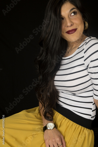 Pretty woman sitting down yellow skirt looking up black backgrou