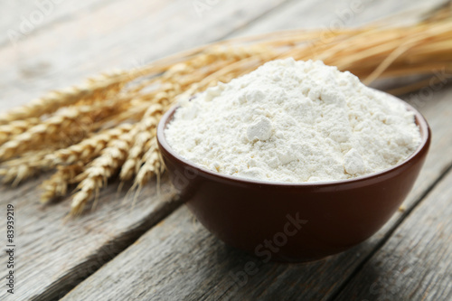 Bowl of wheat flour with spikelets on grey wooden background