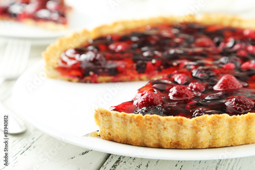 Fresh berry tart on plate on white wooden background