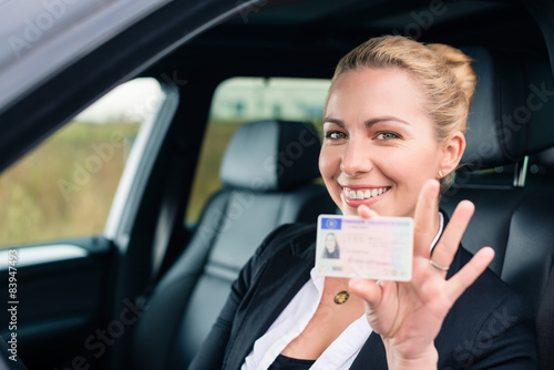 Frau zeigt stolz ihren Führerschein aus dem Auto