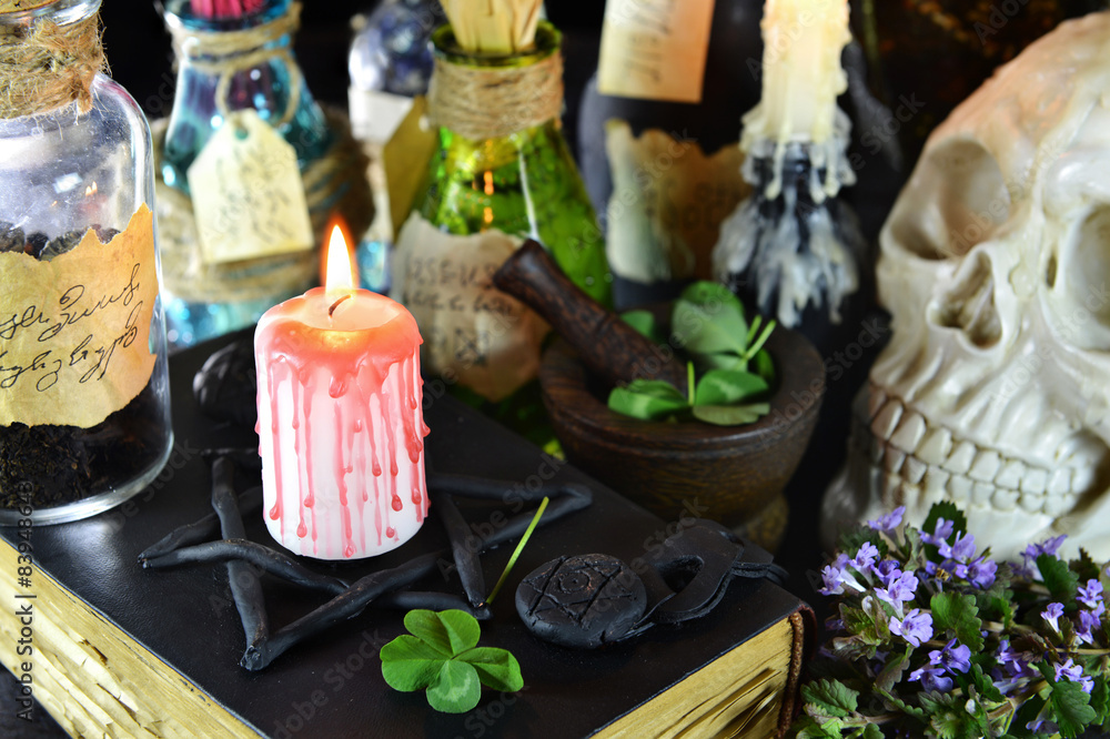 Bloody candle on witch book with magic objects and clover