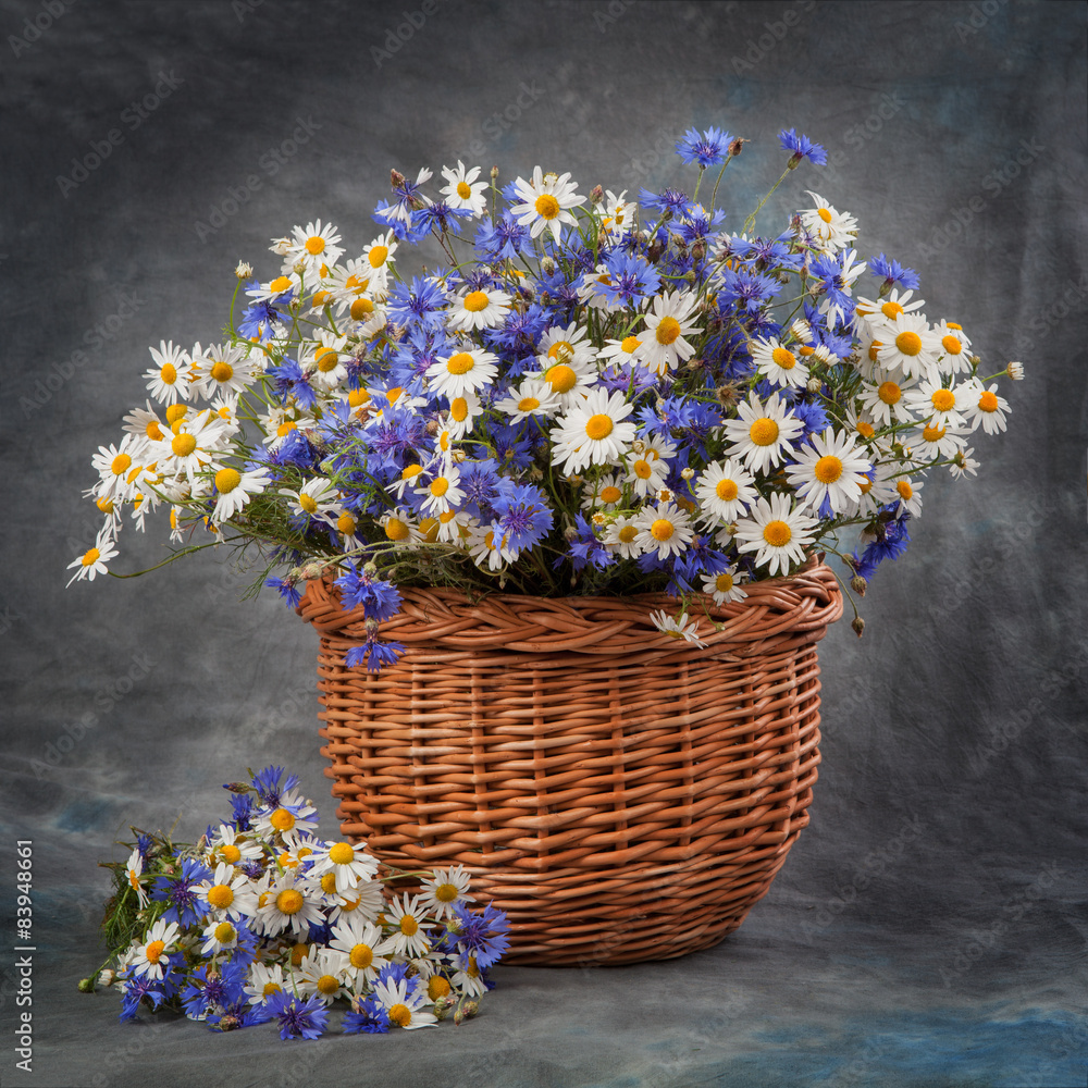 Daisies and cornflowers in a basket on table