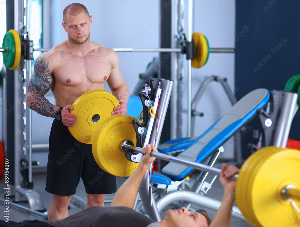 Obraz premium Young man lifting the barbell in gym with instructor