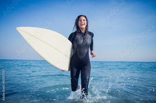 woman in wetsuit with a surfboard on a sunny day