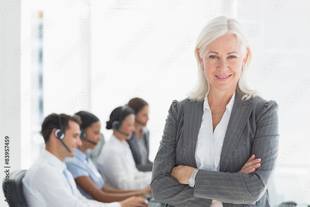 Businesswoman with arms crossed and executives using computers Businesswoman with arms crossed and executives using computers