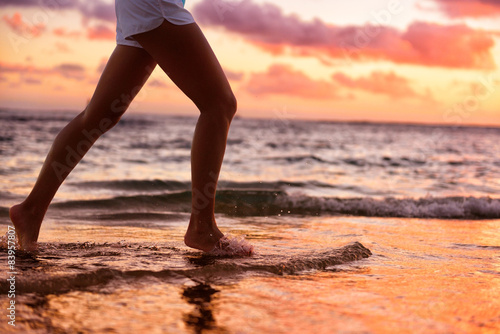 Running woman jogging barefoot in water at beach