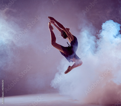 Beautiful young ballet dancer jumping on a lilac background. 