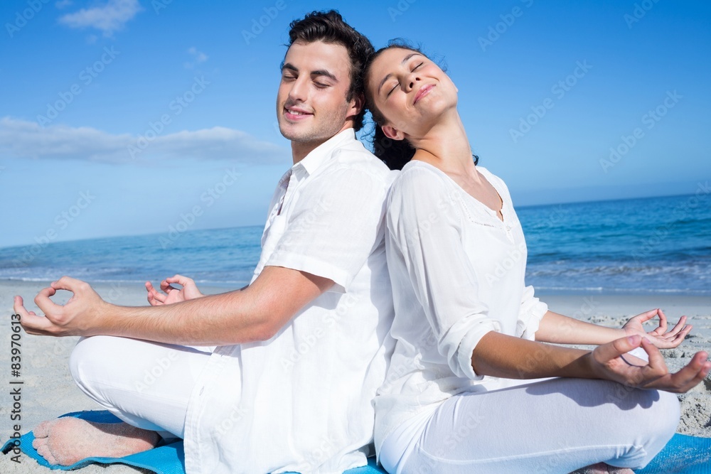 Happy couple doing yoga beside the water