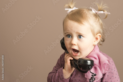 Baby girl in surprise talking on a vintage phone photo