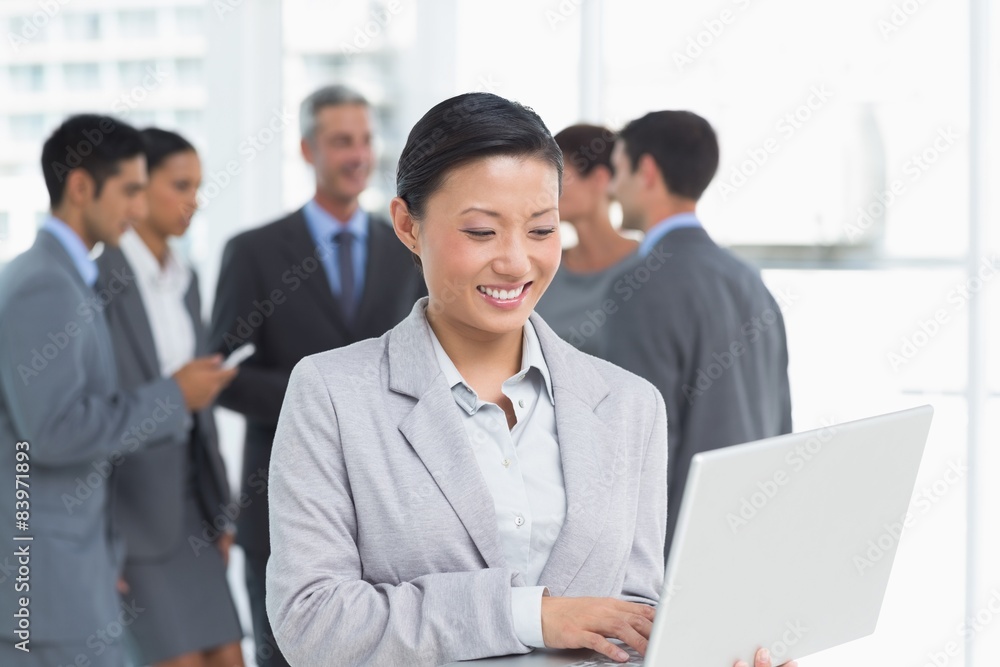 Businesswoman using laptop with colleagues behind Businesswoman using laptop with colleagues behind