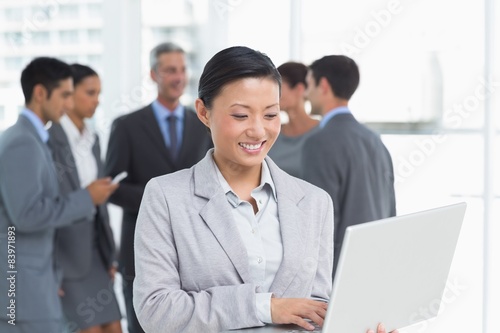 Businesswoman using laptop with colleagues behind
