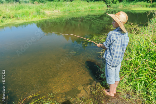 Barefoot fishing boy angling in transparent brownish water body