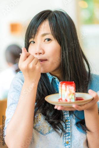 Smiling asian woman eating some strawberry cake in bakery cafe