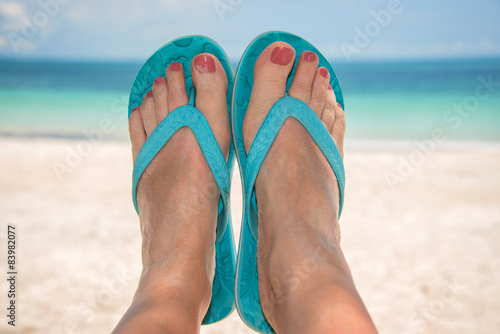 Woman bare sandy feet with blue flip flops, beach and sea 