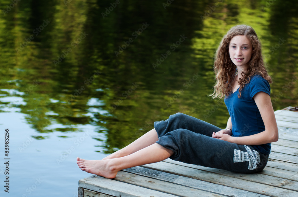 Teenage girl fishing in a lake while sitting on a dock Stock Photo