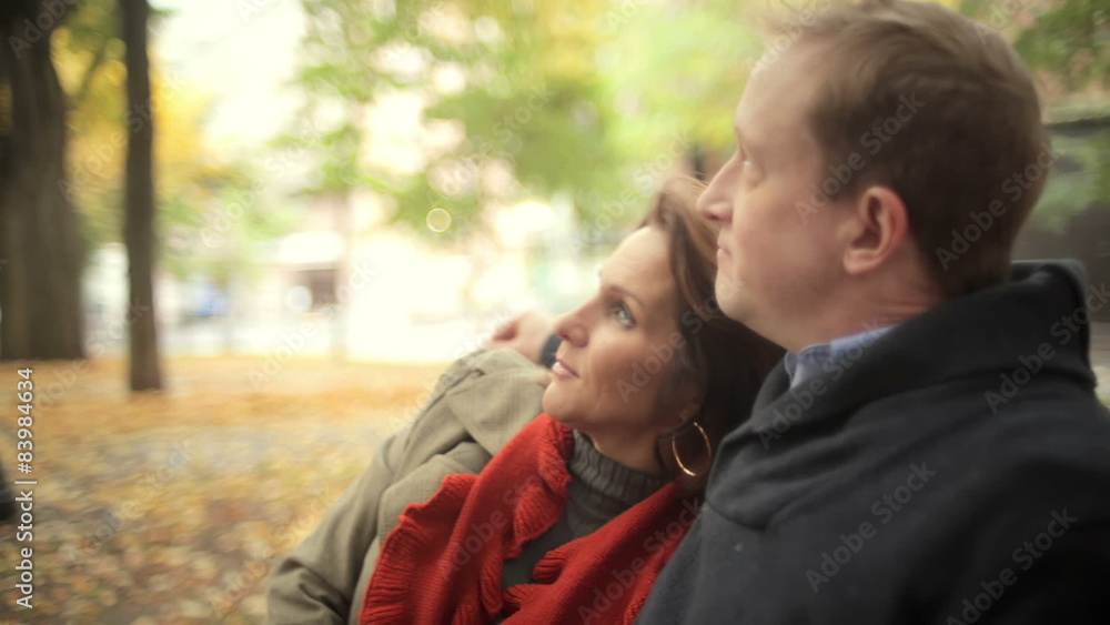 A couple sit at a park bench and embrace each other on a nice fall day A couple sit at a park bench and embrace each other on a nice fall day