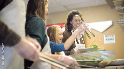A young family works at a soup kitchen helping the homeless by serving them hot food