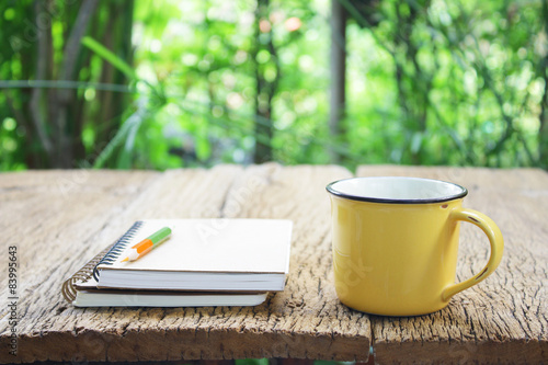 Notebook and coffee in yellow cup on wooden table