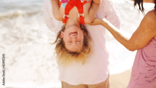 Little girl on her dad's shoulders gets tickled by her mom. 