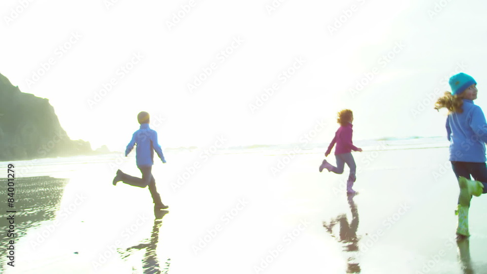 Three kids run down the beach with a bright sun shining on them and the shore Three kids run down the beach with a bright sun shining on them and the shore
