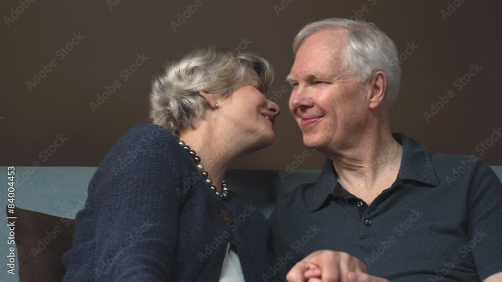 An older man gets a kiss on the cheek from an older woman on a couch An older man gets a kiss on the cheek from an older woman on a couch
