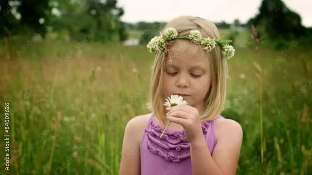 A blonde girl stands in a field and smells a flower during the day A blonde girl stands in a field and smells a flower during the day