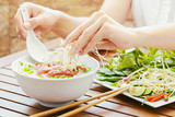 Young woman sprinkles sprouts to the Pho Bo in Vietnamese cafe