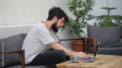 young tattooed guy using a laptop and a smartphone photo