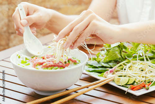Young woman sprinkles sprouts to the Pho Bo in Vietnamese cafe