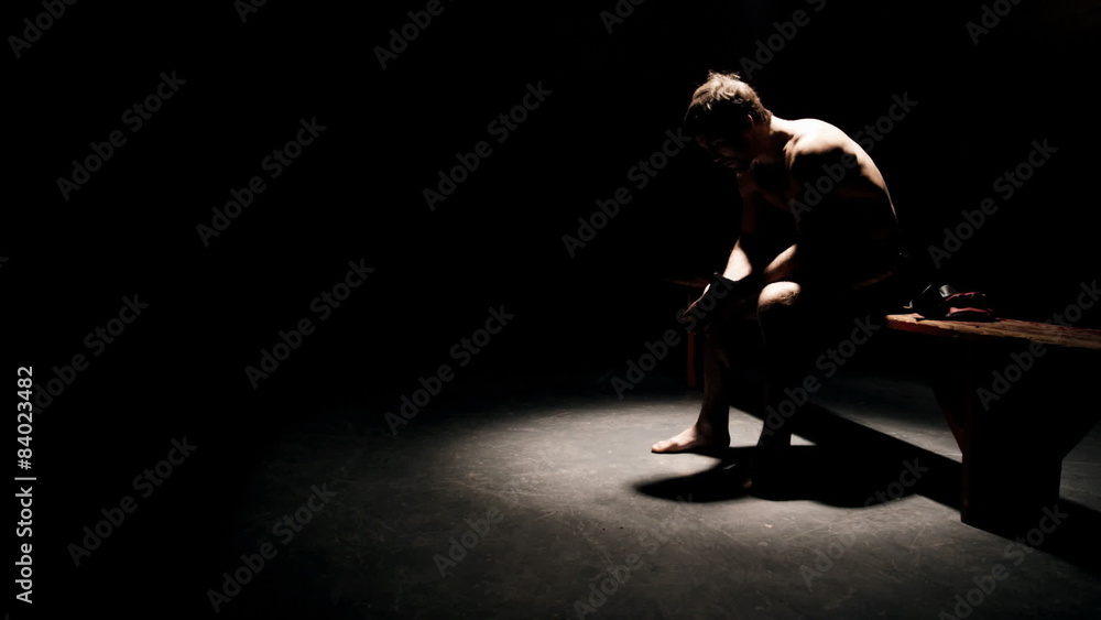 A fighter sits on bench under a light in the dark prepping himself mentally for his fight A fighter sits on bench under a light in the dark prepping himself mentally for his fight