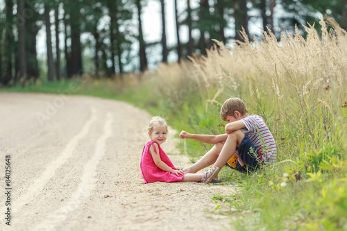 Sibling children playing in dust sitting on summer dirt road