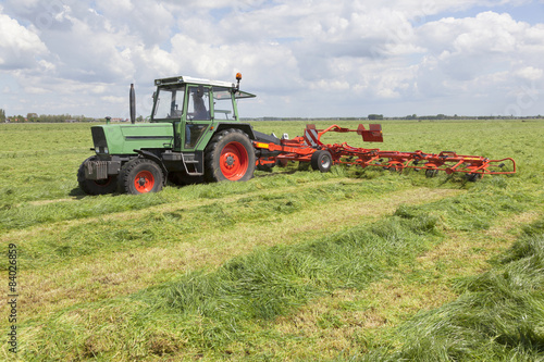 red hay turner in green meadow in the netherlands
