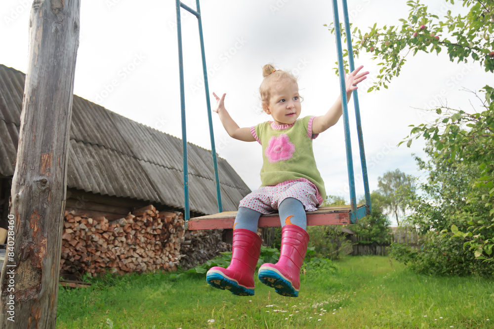 Toddler girl wearing red gumboots riding on handmade swing