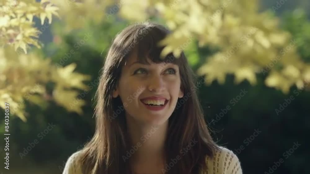 Young woman standing under a tree looks at the camera and smiles Young woman standing under a tree looks at the camera and smiles