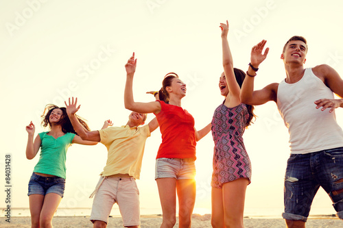 smiling friends dancing on summer beach